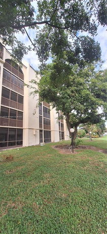Front view of a multi-story building with screened balconies and surrounding green lawn.