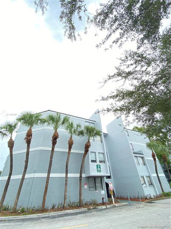 Front view of a multi-story building with rounded architectural features and several palm trees.