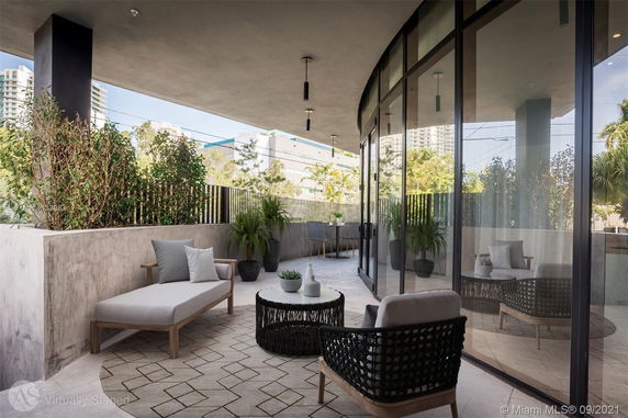 Outdoor terrace with seating and plants, adjoining a glass-walled building.