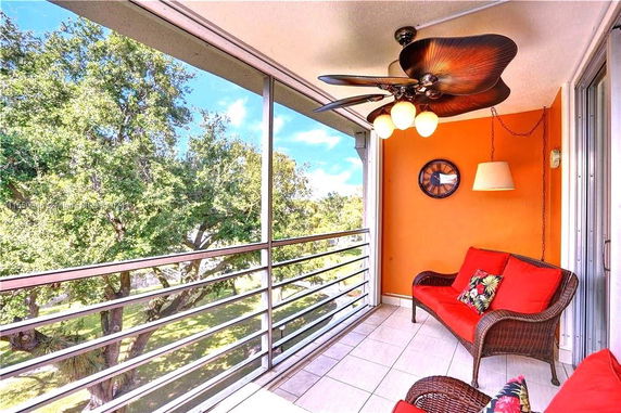 Balcony with orange wall, wicker furniture, and ceiling fan, overlooking trees.