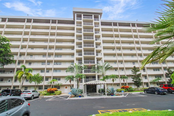 Front view of a multi-story apartment building with balconies and parking area.