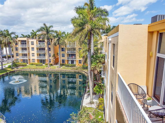 View of a multi-story apartment building next to a pond with a fountain.