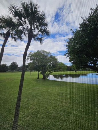 View through a screen of a grassy area with trees and a pond.