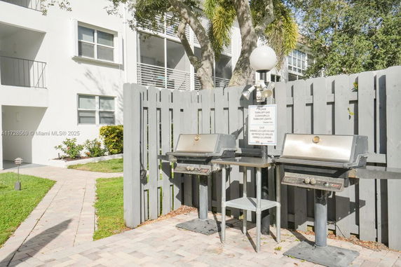 Front view of a multi-story residential building with a fenced area containing grills.