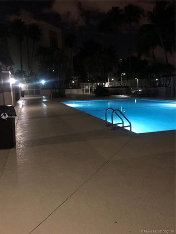 Nighttime view of a well-lit outdoor swimming pool with surrounding seating area.