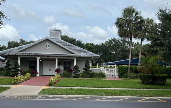 Front view of a single-story building with a gabled roof and decorative plants.