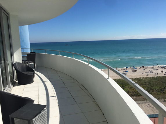 View of a beach and ocean from a curved balcony with seating.