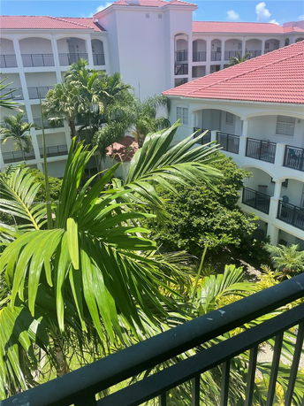 View from a balcony overlooking a multi-story building with red-tiled roofs and surrounding greenery.