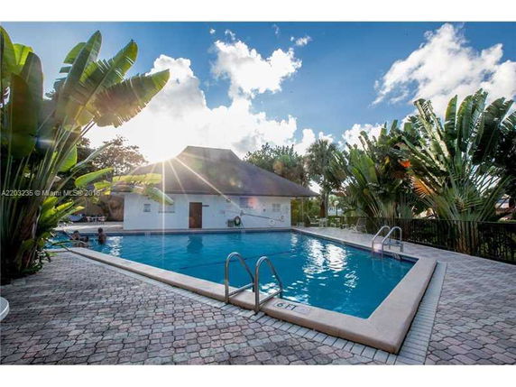Outdoor swimming pool surrounded by tropical plants and a small building.