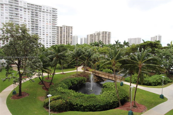 View of high-rise buildings with a landscaped garden including a small pond and palm trees.