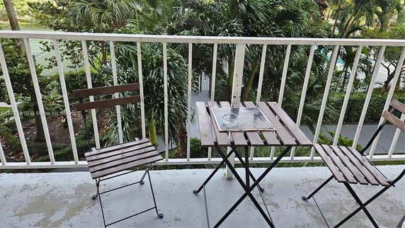 View from a balcony with a wooden table and chairs overlooking greenery and outdoor areas.