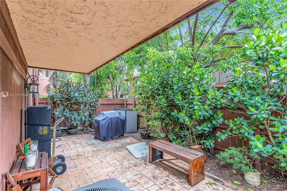 Outdoor patio area with a wooden fence, plants, a grill, and a wooden bench.