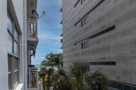 View between two buildings with a glimpse of palm trees and the ocean in the distance.