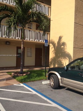 Front view of a multi-story building with balconies and a parking area.