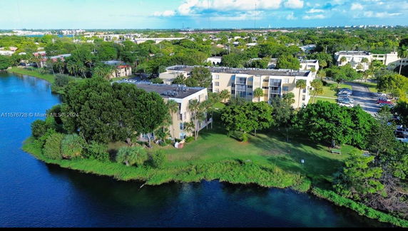 Aerial view of a multi-story building complex near a body of water with surrounding greenery.