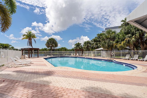 Outdoor swimming pool area with lounge chairs and palm trees.