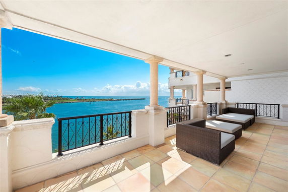 Covered outdoor terrace with lounge seating overlooking a large body of water.