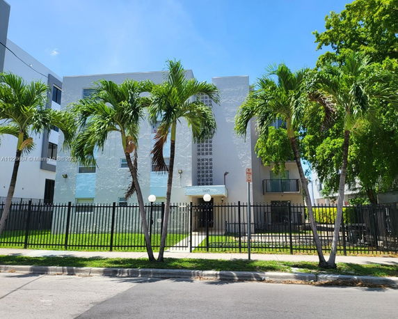 Front view of a multi-story building with palm trees and a fenced entrance.