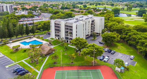 Aerial view of a multi-story apartment building with a swimming pool and tennis court, surrounded by greenery.