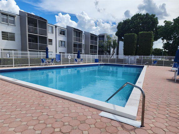 Outdoor swimming pool surrounded by a fence in front of a multi-story residential building.