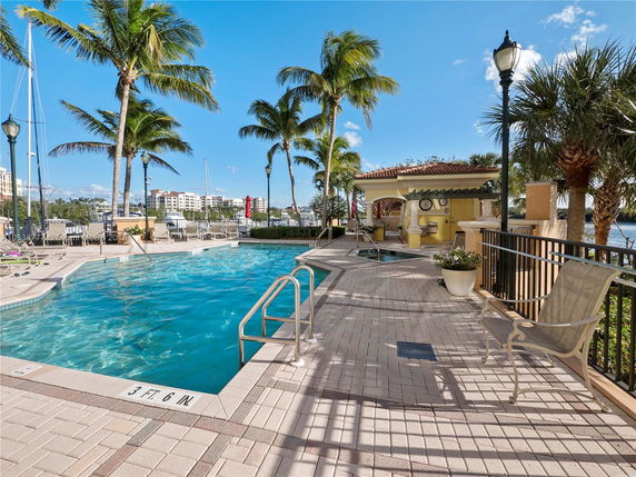 View of a pool area with palm trees, and a partial view of nearby buildings in the background.