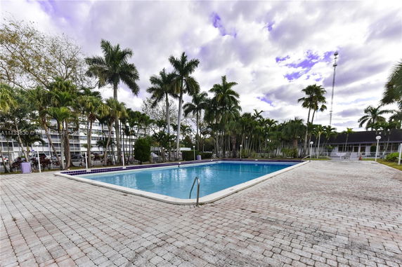 Outdoor swimming pool area surrounded by palm trees and building structures.