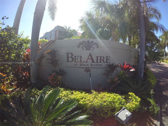 Front view of a sign that reads 'Bel Aire at Boca Raton' surrounded by tropical plants.