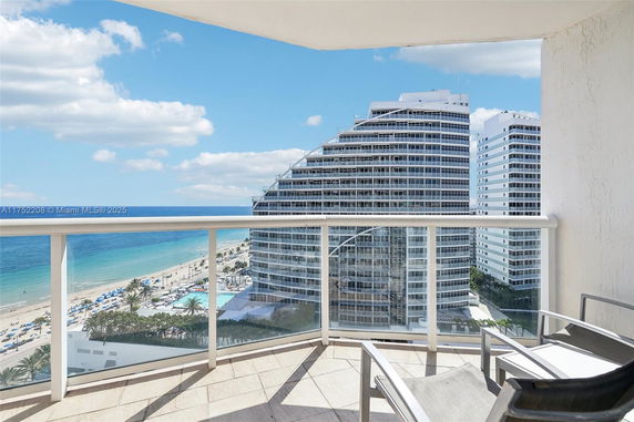 Panoramic view from a balcony overlooking the ocean and nearby high-rise buildings.
