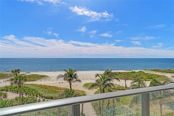 Panoramic view of the ocean and beach from a balcony with palm trees and blue sky.