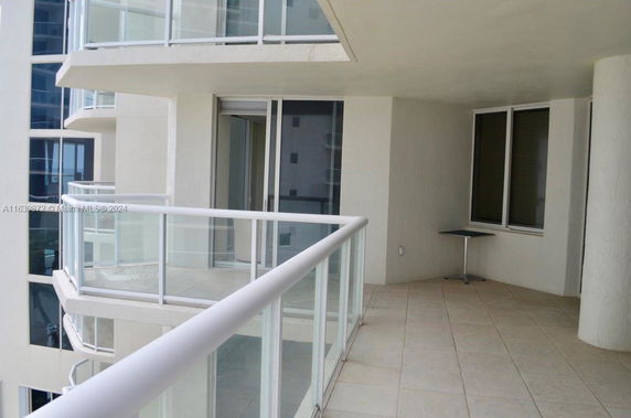 Balcony of a multi-story apartment with glass railings and sliding doors.