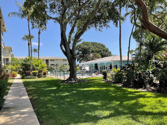 View of surrounding area with several buildings and a swimming pool, surrounded by trees and lawn.