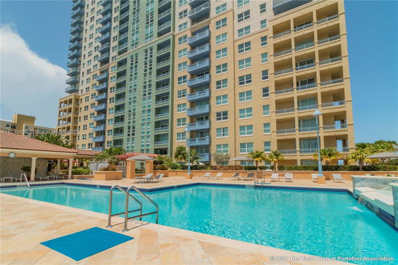 Front view of a tall residential building with multiple balconies overlooking a swimming pool area.