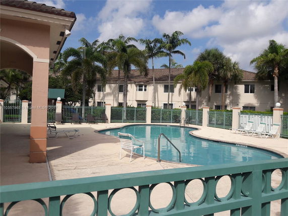 Outdoor swimming pool area with lounge chairs and a fence surrounding it.