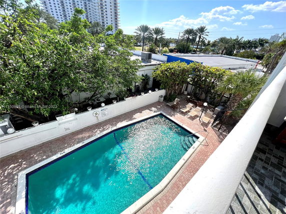 View of an outdoor swimming pool surrounded by a brick patio and lush greenery.