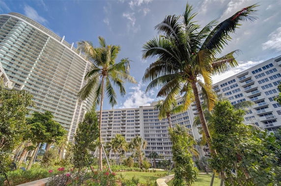 View of tall, modern residential buildings with balconies surrounded by palm trees and greenery.