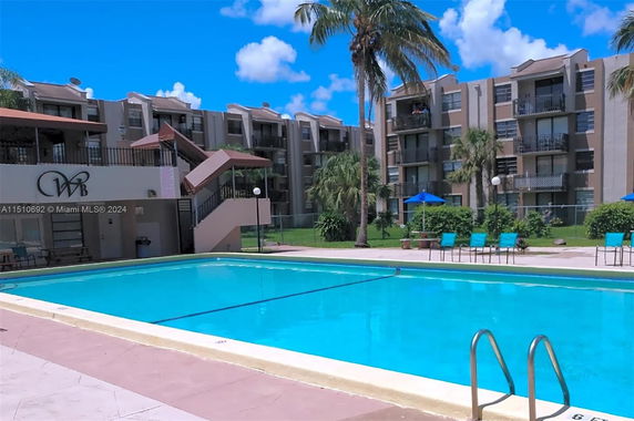 Outdoor swimming pool area in front of a multi-story residential building.