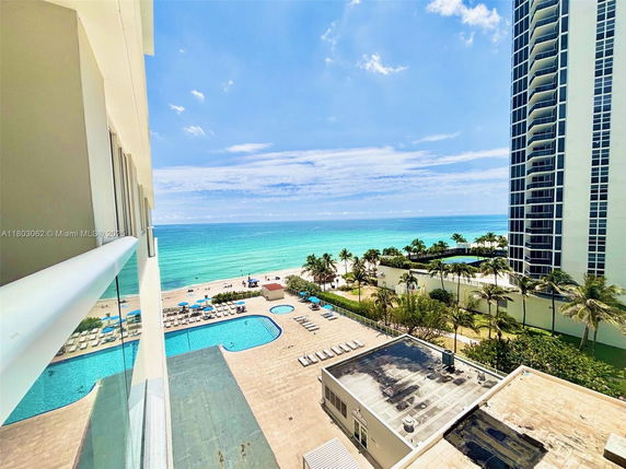 Panoramic view of a beach and ocean from a building, with a swimming pool and lounge area visible.