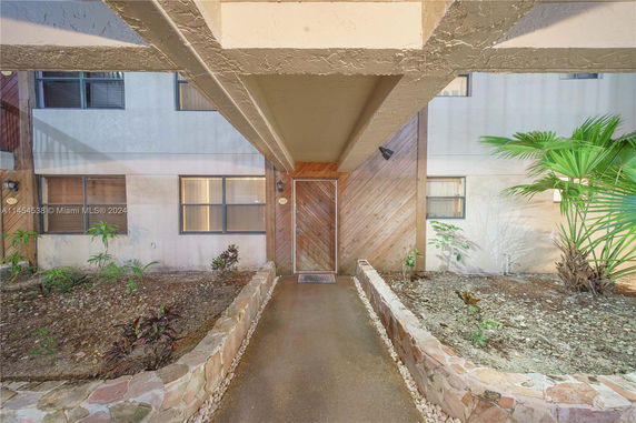 Entrance view of a building with a pathway and stone-bordered garden beds.