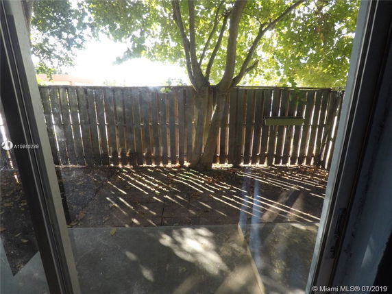 View of a fenced outdoor area with a tree and paved ground seen from a window.