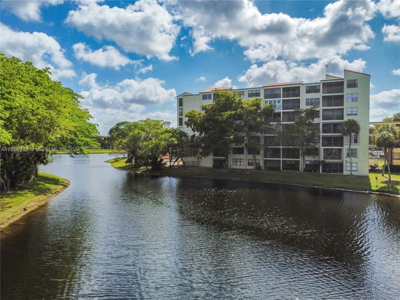 View of a multi-story residential building by a water body with trees.