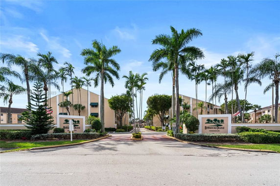 Front view of a condominium complex with palm trees lining the entrance.