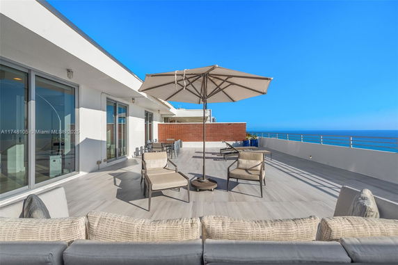Spacious rooftop terrace with modern outdoor furniture and a large umbrella, offering views of the ocean.