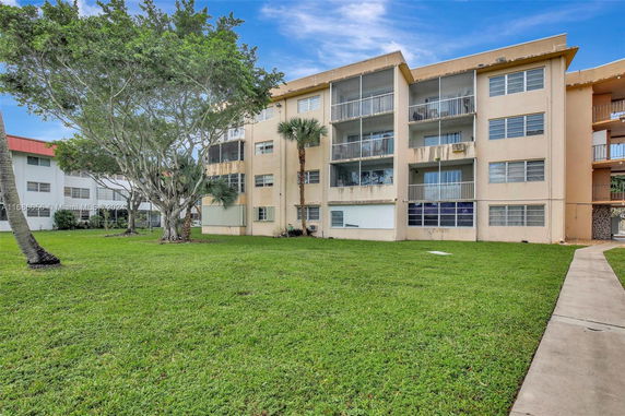 Rear view of a multi-story residential building with balconies and grassy lawn.