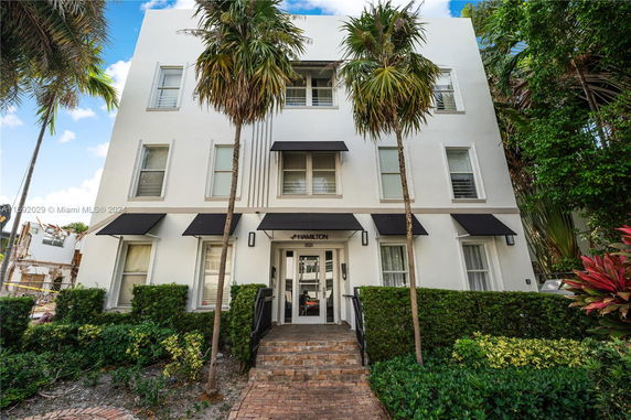 Front view of a multi-story building with plants and awnings.