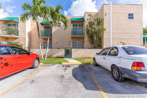 Outdoor parking area in front of a two-story building with green awnings and balconies.