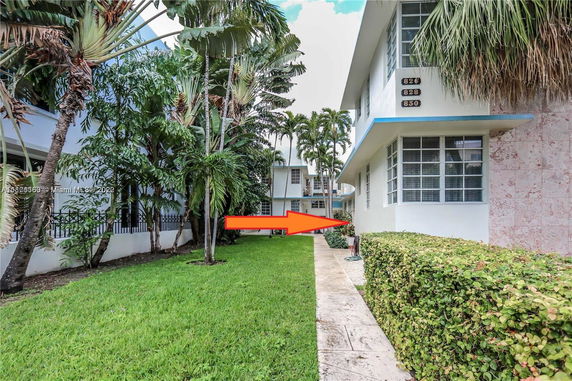 View of the side exterior of a building with multiple floors and large windows, surrounded by tropical vegetation.