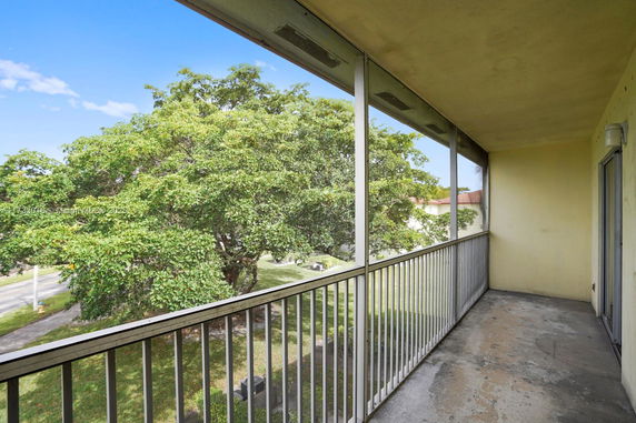 View from a balcony with metal railing, overlooking a large tree and open outdoor space.