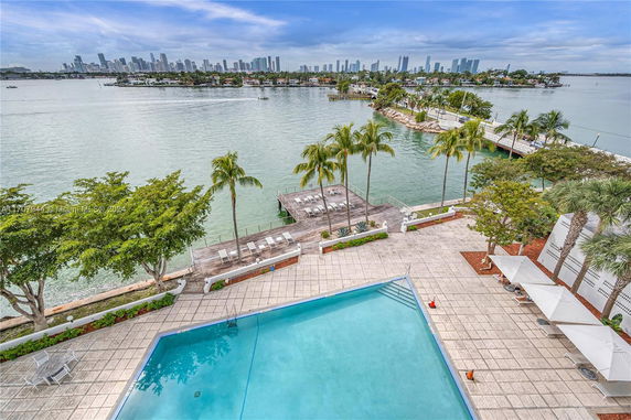 Wide angle view of a pool area overlooking the water with a distant skyline.
