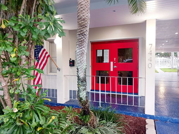 Front view of a building entrance with red double doors and a flag.