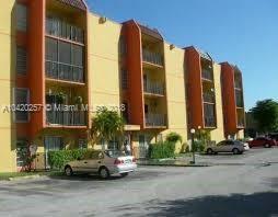 Front view of a four-story apartment building with balconies and a parking area.